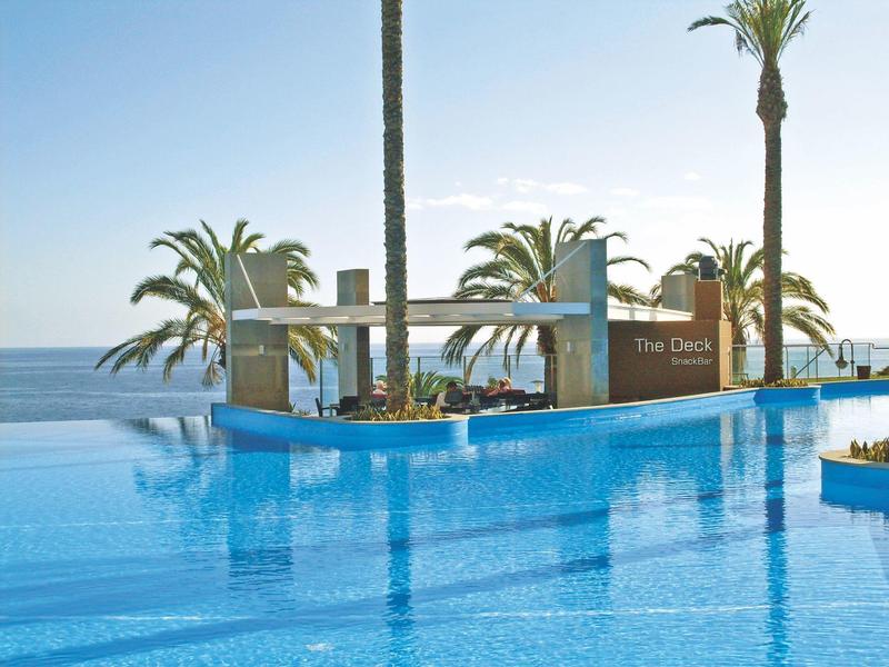 Moderner Infinity-Pool mit Meerblick und Palmen unter klarem blauem Himmel.