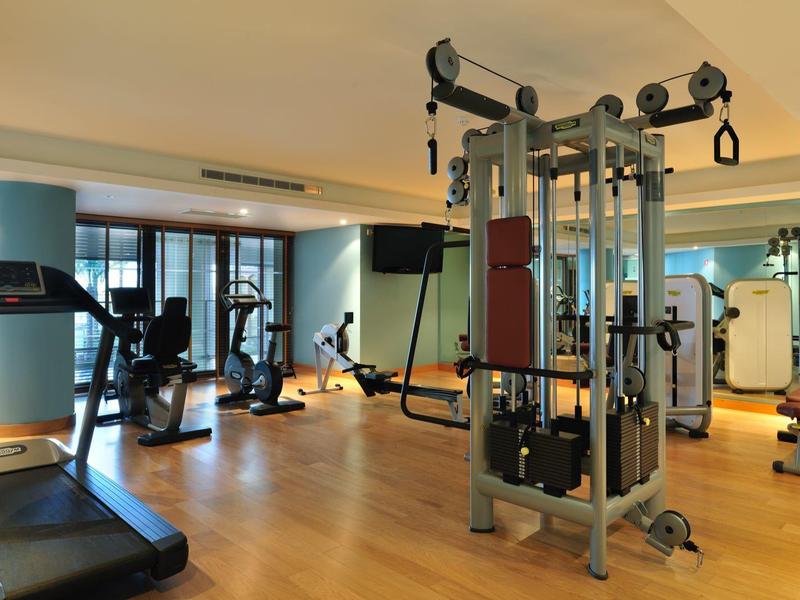 Heller Fitnessraum mit modernen Trainingsgeräten und Holzfußboden.