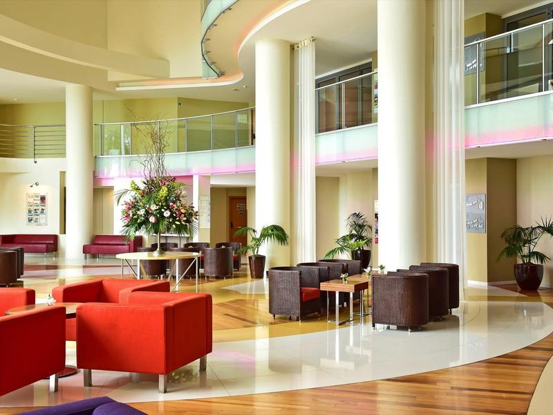 Helle und moderne Hotellobby mit roter und brauner Sitzgruppe und großen weißen Säulen.