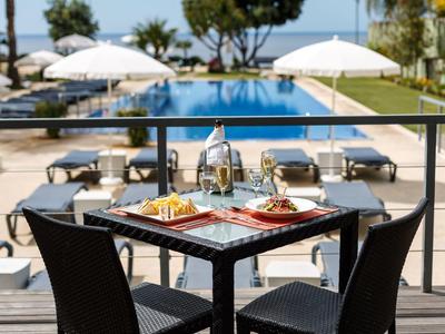 Ein gedeckter Tisch mit Essen und Getränken am Balkon, Blick auf Pool und Strand im Hintergrund.