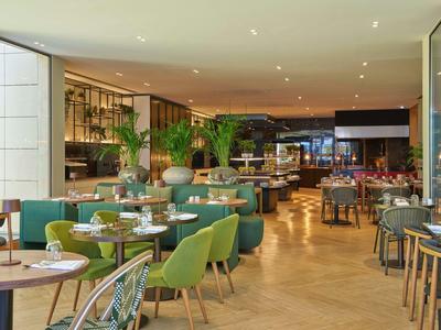 Modernes Restaurant mit grünen Stühlen, runden Tischen und hellem Holzboden, freundlich eingerichtet.