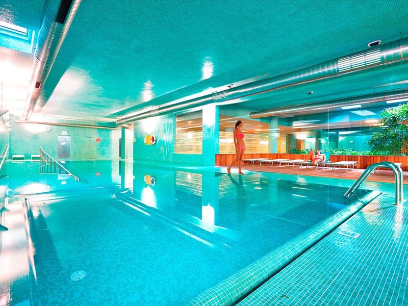 Piscina interna con piastrelle blu, scivolo d'acqua e finestre panoramiche in un hotel
