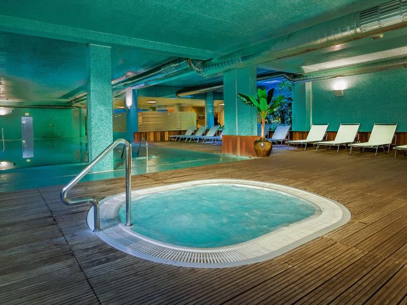 Idromassaggio interno accogliente con lettini e piscina sullo sfondo.