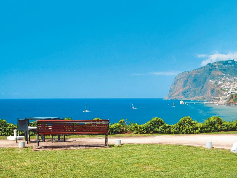 Panchina vicino al mare con vista su acqua blu e montagne sotto un cielo sereno
