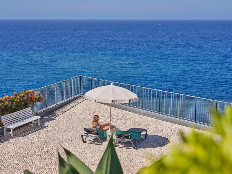Persona che si rilassa su una sdraio con ombrellone su una terrazza con vista sul mare.