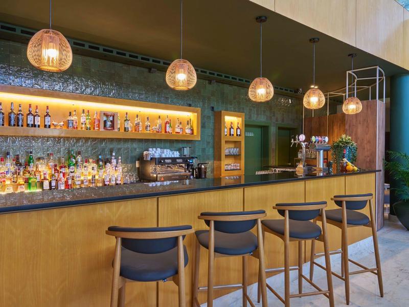 Bar moderna dell'hotel con bancone in legno, otto sgabelli e lampade a sospensione calde.