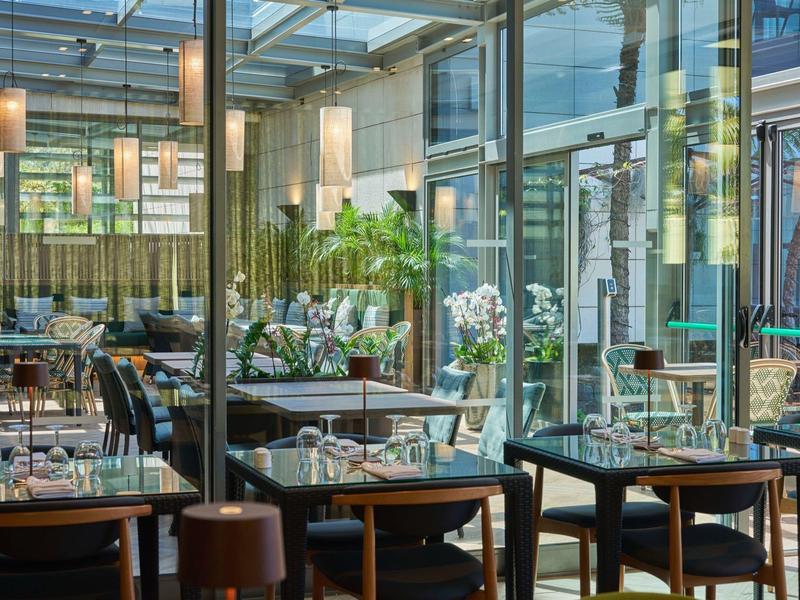 Ristorante moderno con pareti di vetro, tavoli in legno e composizioni floreali all'interno.