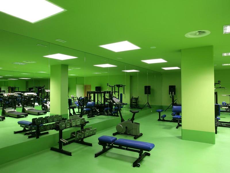 Palestra moderna con pareti verdi, specchi e panche da allenamento blu.