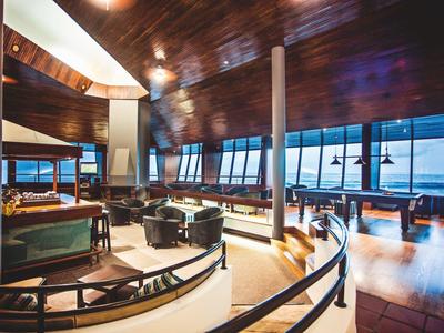 Lounge di hotel di lusso con soffitto in legno, grandi finestre con vista sull'oceano e area salotto moderna.