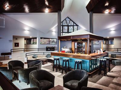 Lobby moderna dell'hotel con bar centrale, sgabelli turchesi e poltrone scure intorno ai tavoli.