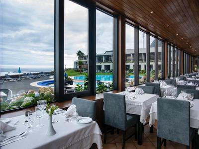 Luminoso ristorante con grandi finestre affacciate sulla piscina, giardino e vista mare dell'hotel.