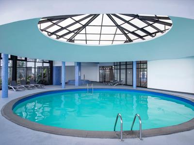 Piscina rotonda interna con tetto di vetro e scaletta in hotel moderno.