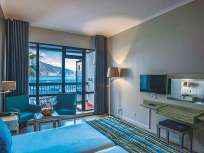 Camera d'hotel moderna con vista mare, balcone, letto accogliente e illuminazione elegante.