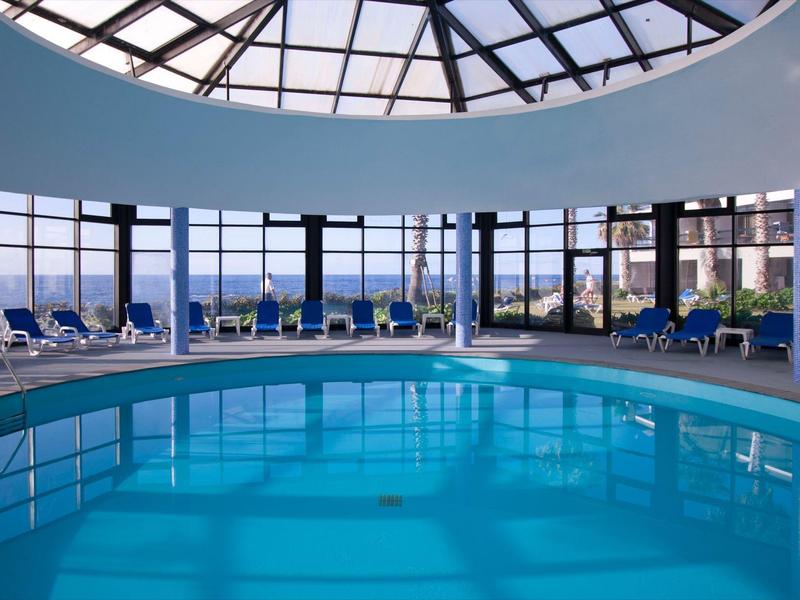 Piscina coperta con grande tetto a cupola di vetro e molte sdraio in hotel.