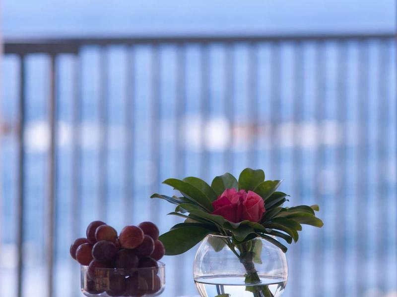 Ciotola di vetro con fiori e dessert su un tavolo bianco con vista mare.