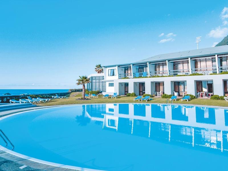 Hotel fronte oceano con grande piscina azzurra e sedie a sdraio sotto un cielo limpido.