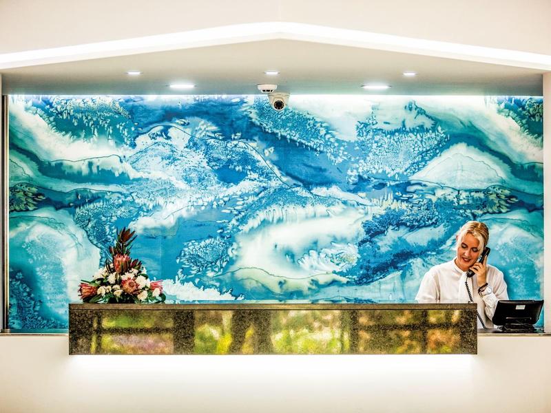 Reception dell'hotel con banco moderno e opera d'arte oceanica sullo sfondo.