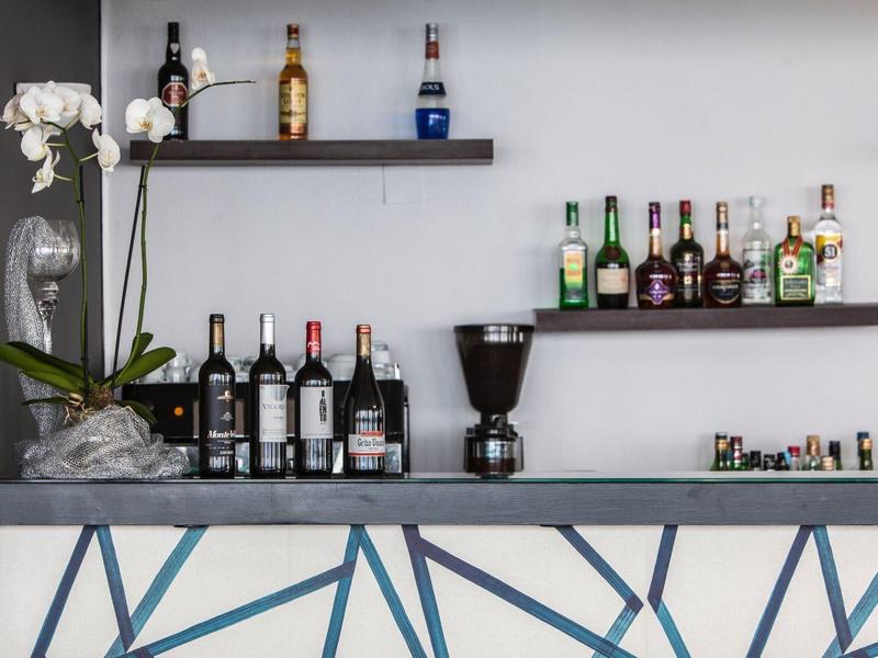 Bancone bar con bottiglie di vino, liquori, macinacaffè e una pianta di orchidea bianca.