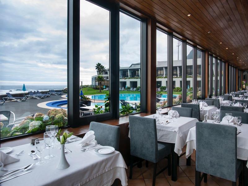 Luminoso ristorante con grandi finestre affacciate sulla piscina, giardino e vista mare dell'hotel.