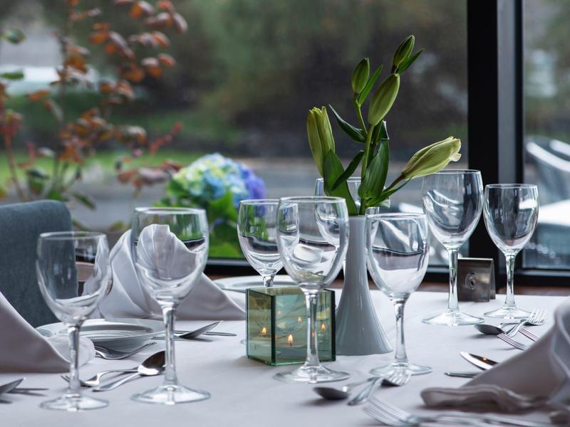 Tavola da pranzo elegante con bicchieri, tovaglioli e una piccola pianta vicino alla finestra.