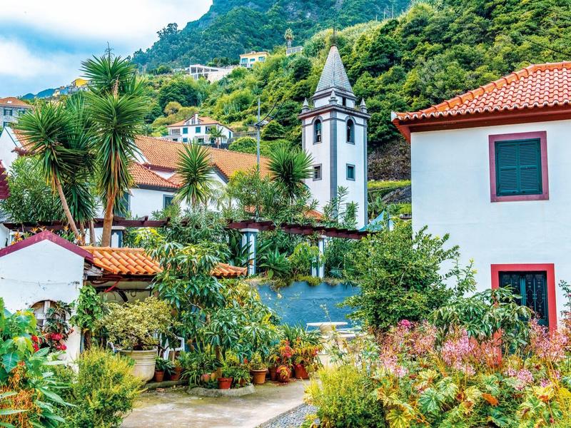 Villaggio pittoresco con case bianche, tetti rossi e vegetazione rigogliosa su una collina.