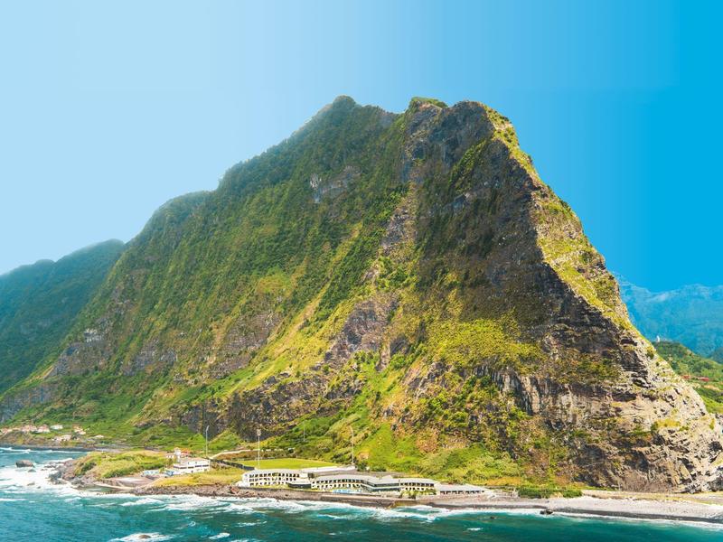 Un'isola rocciosa con pendii verdi e acqua blu chiara in primo piano.