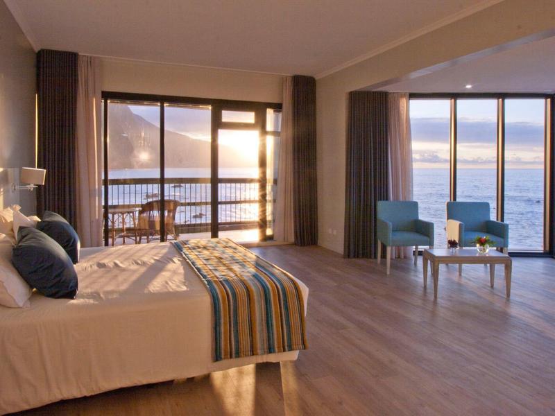 Ampia camera d'hotel con grandi finestre che si affacciano sul mare e pavimento in legno.