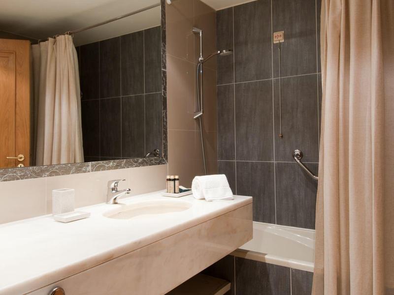 Bagno moderno con grande specchio, lavabo bianco e tenda doccia beige.