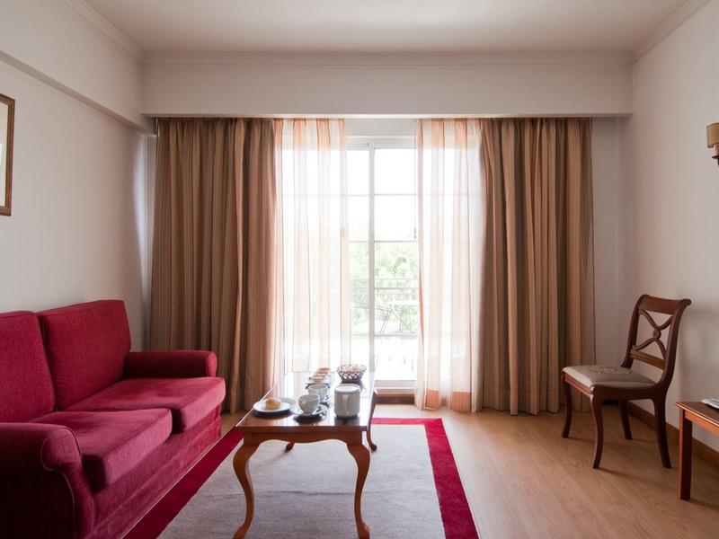 Accogliente soggiorno con divano rosso, sedia in legno e un piccolo tavolo davanti a una grande finestra.