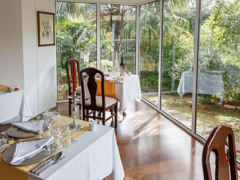Ristorante elegante con tovaglie bianche e grandi finestre che si affacciano su un giardino.