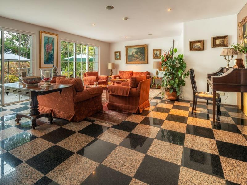 Soggiorno luminoso con pavimento a scacchiera, mobili imbottiti arancioni e un pianoforte.