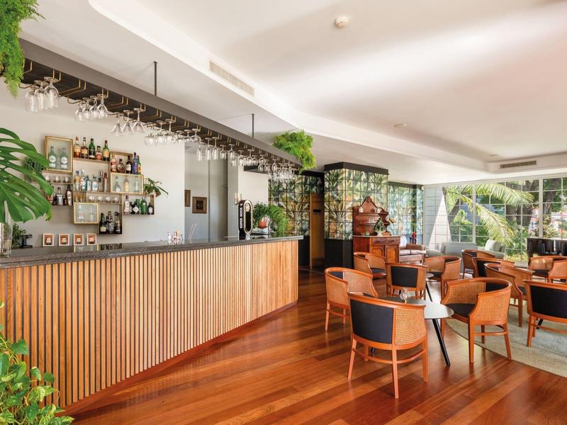 Area bar moderna con bancone in legno, sedie e grandi finestre con vista sullo spazio esterno.