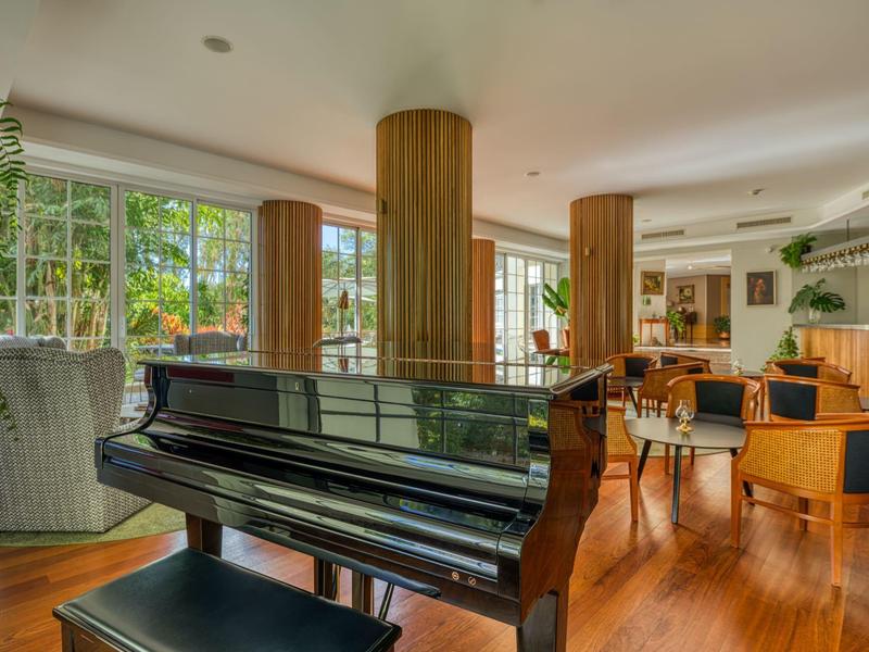 Elegante pianoforte nero in un lounge d'hotel luminoso e moderno con sedie e grandi finestre.
