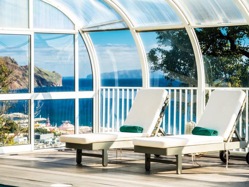 Due sdraio con cuscini in una stanza di vetro con vista sul mare.