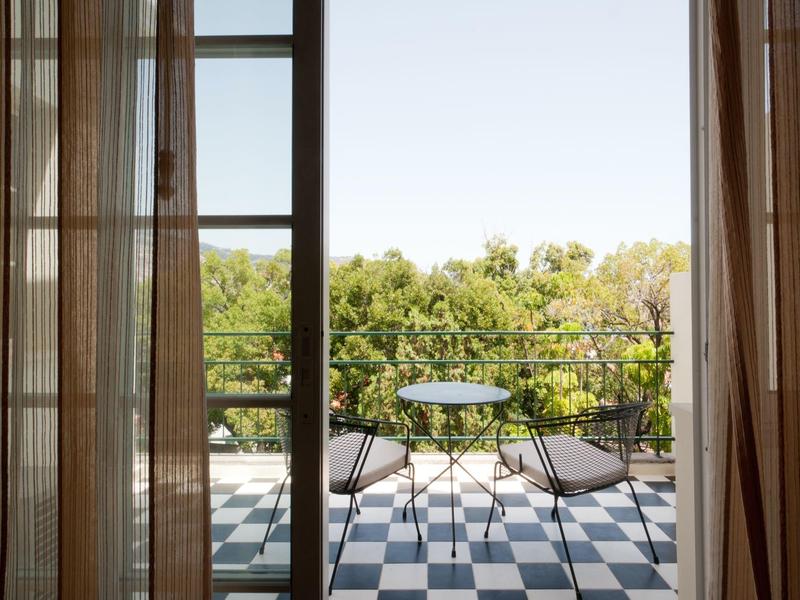 Balcone con piccolo tavolo e due sedie che si affaccia su alberi verdi e cielo blu.