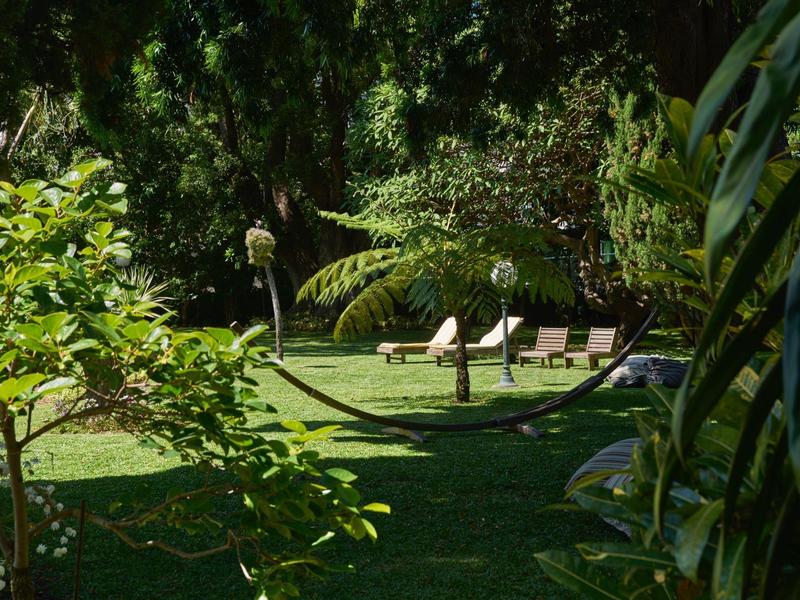 Giardino verde con sdraio e ombrellone in un paesaggio soleggiato.