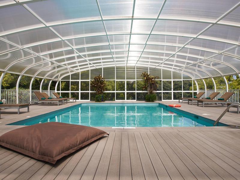 Piscina coperta con cupola di vetro, terrazza in legno e lettini.
