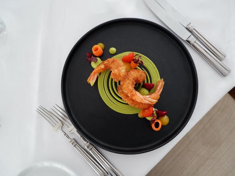 Piatto elegante con gamberi su piatto nero, decorato con salsa verde e piccoli accenti colorati.