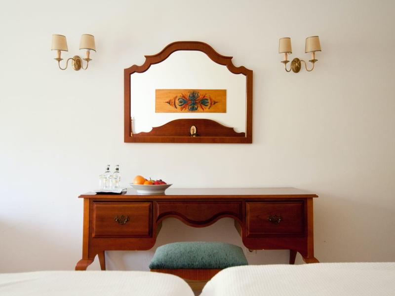 Scrivania in legno con sgabello verde, specchio sopra e due lampade da parete in una stanza d'hotel.