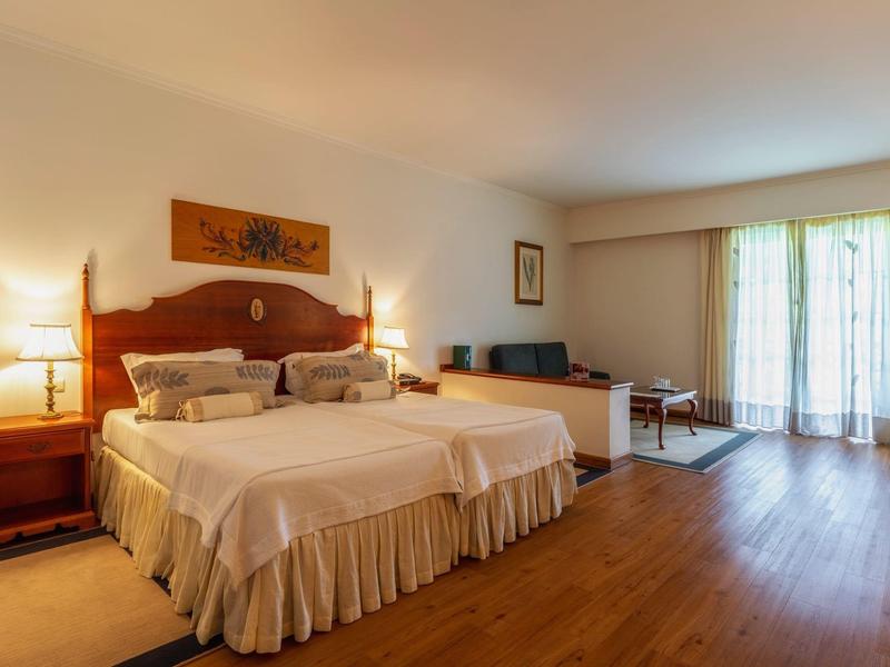 Camera d'hotel accogliente con due letti matrimoniali, pavimento in legno e balcone con vista esterna.