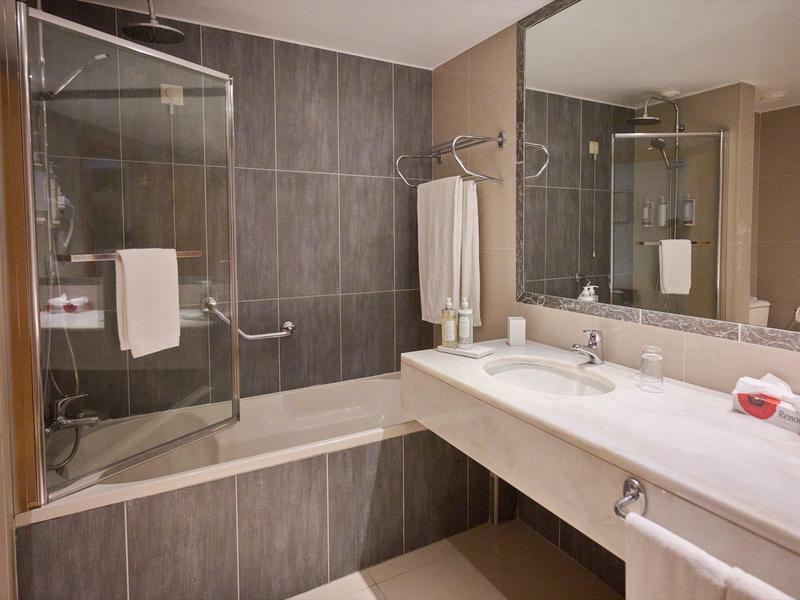 Bagno moderno con vasca da bagno, doccia in vetro, grande specchio e lavandino bianco.