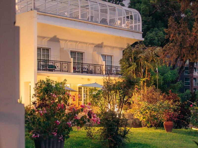 Hotel illuminato con balcone e giardino curato al crepuscolo.