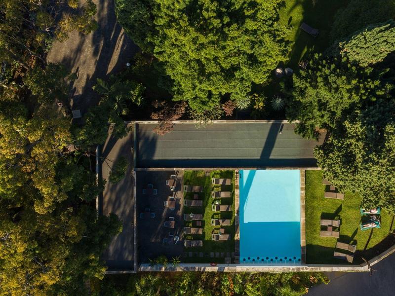 Vista aerea di una piscina rettangolare accanto ad alberi e un giardino con sedie a sdraio.