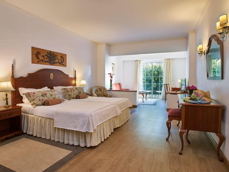 Elegante camera d'hotel con due letti singoli, scrivania, sedie e vista sul balcone.