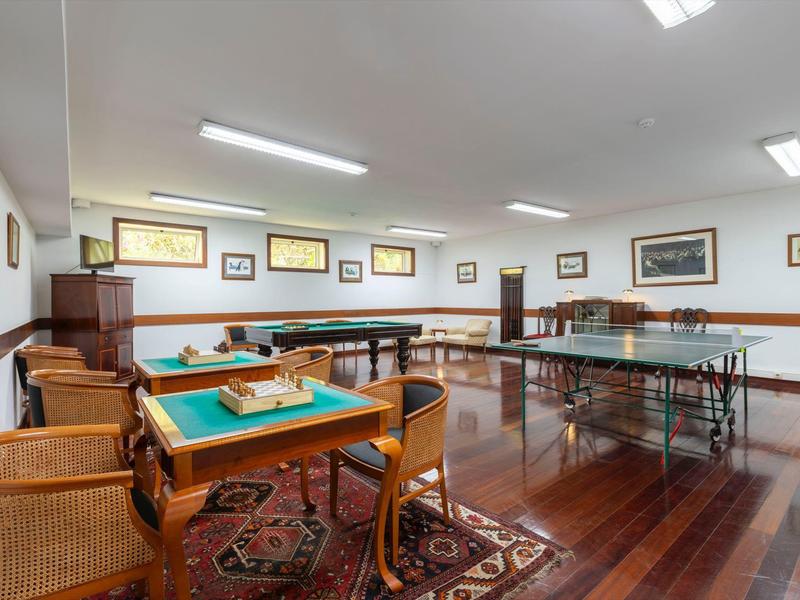 Una stanza luminosa per giochi e socializzazione con tavoli e sedie su pavimenti in legno e tappeti.