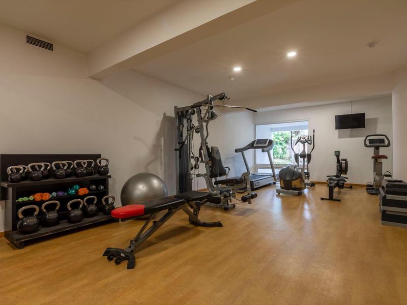 Palestra moderna con attrezzature, manubri e pavimento in legno in un hotel.