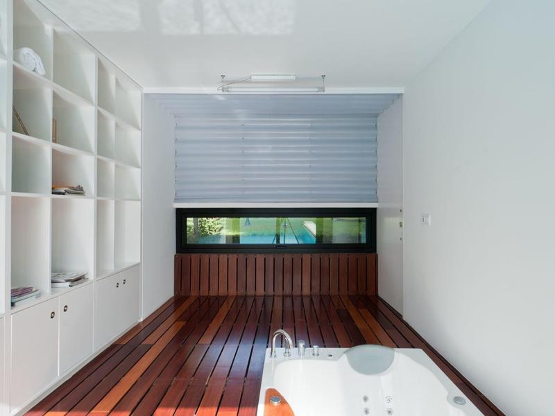 Area benessere moderna con pavimento in legno, vasca da bagno e scaffali bianchi a parete.