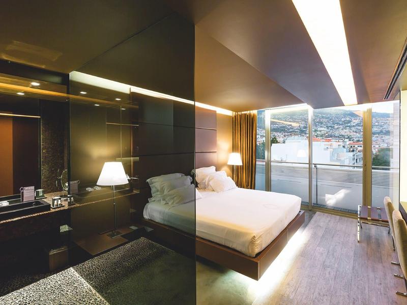 Chambre d'hôtel moderne avec grand lit, bureau, placard miroir et balcon avec vue sur la mer.