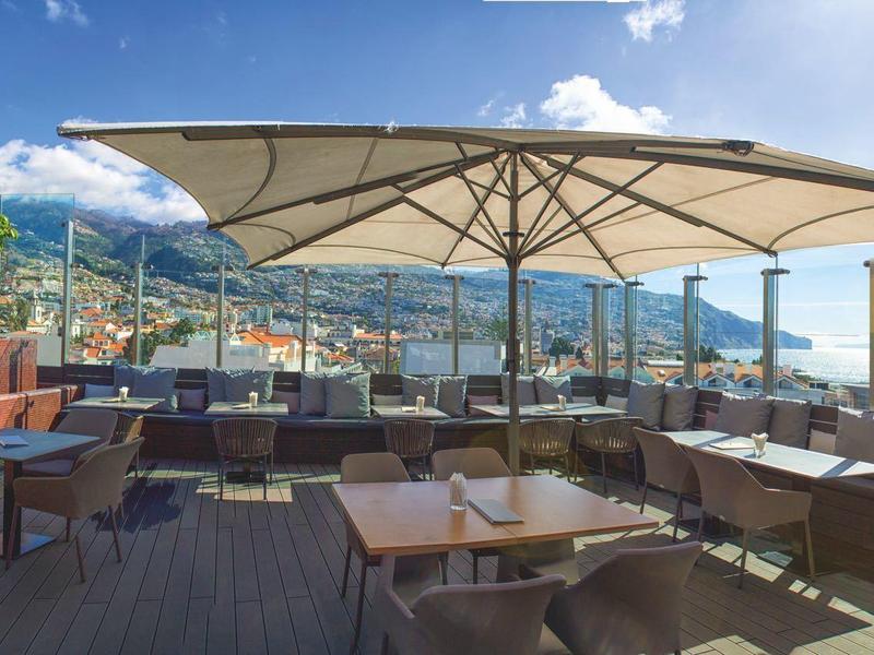 Terrasse sur le toit avec sièges sous des parasols avec vue sur la mer et les montagnes.