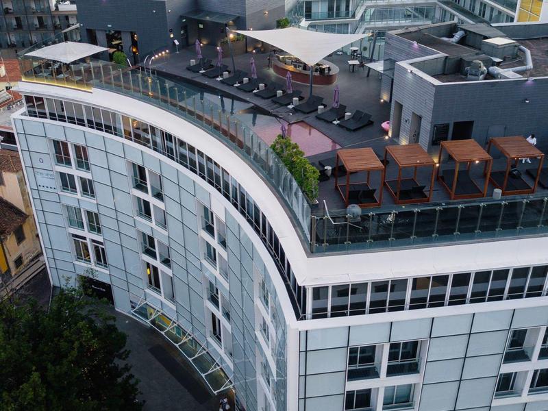 Hôtel moderne avec design incurvé et terrasse sur le toit dans un cadre urbain verdoyant.